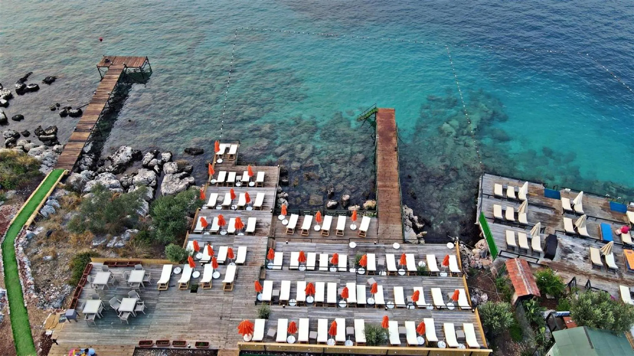 Terrasse en bois avec transats et parasols au bord de l'eau turquoise.