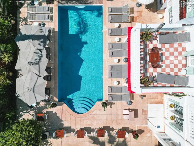 Vue aérienne d'une piscine rectangulaire entourée de chaises longues et de parasols.