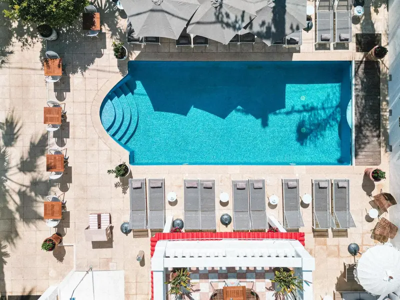 Vue aérienne d'une piscine rectangulaire entourée de transats et de parasols.