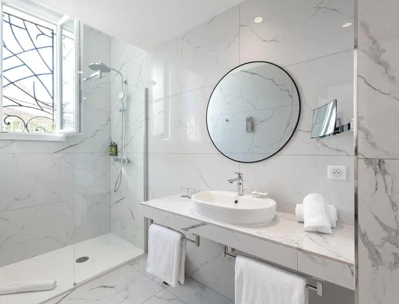 Une salle de bain moderne avec douche à l'italienne et grand miroir rond.