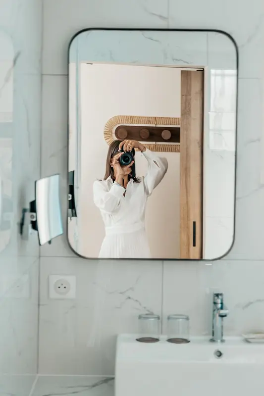 Une personne se photographie devant un miroir dans une salle de bain claire.