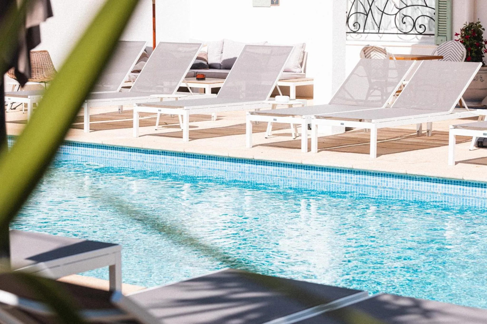 Transats blancs disposés autour d'une piscine carrelée bleu clair.