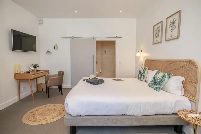 Une chambre lumineuse avec un lit recouvert d'une courtepointe blanche et des coussins verts.