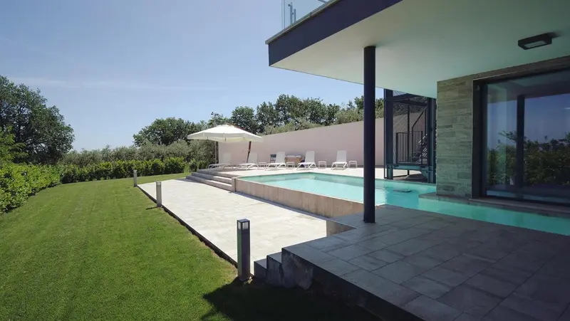 Une piscine rectangulaire bordée d'une terrasse ensoleillée et d'une pelouse verdoyante.