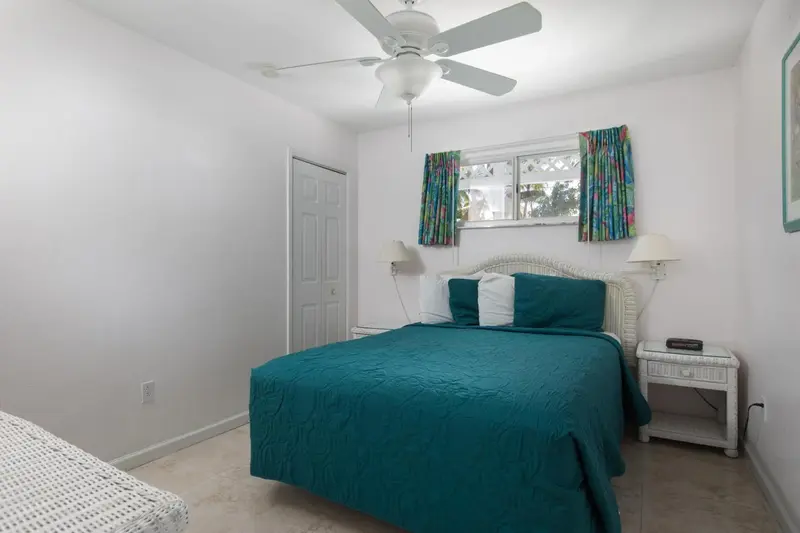 Une chambre lumineuse avec un lit recouvert d'une couverture turquoise et des rideaux fleuris.