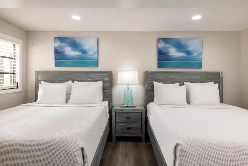 Deux lits simples avec des couvertures blanches et des tableaux abstraits au-dessus.