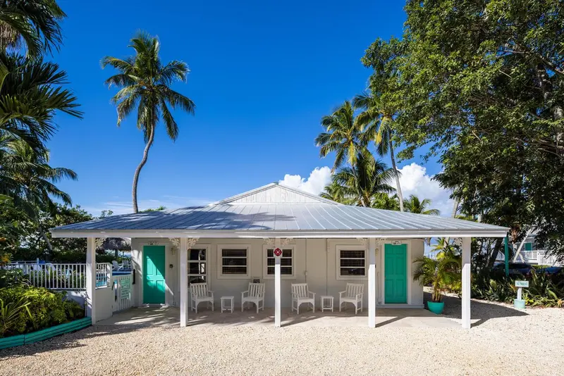 Façade d'un bâtiment blanc avec des portes turquoise et des chaises sur une terrasse.