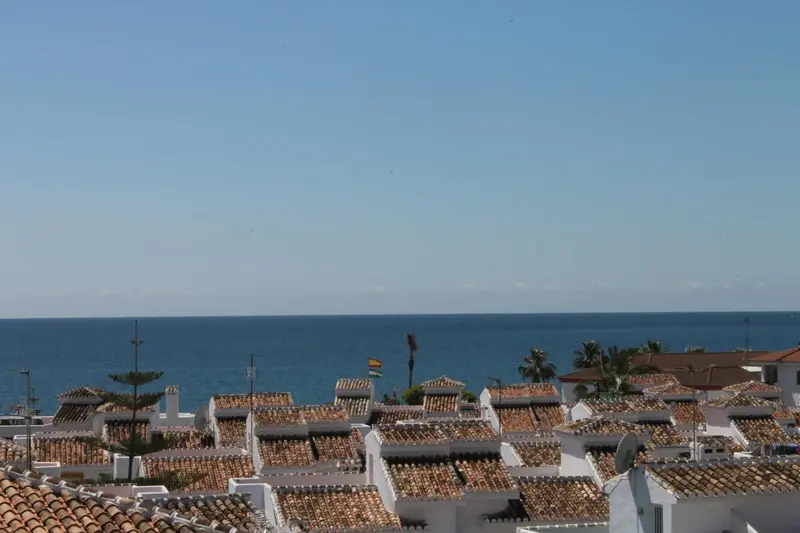 Toits blancs et vue sur la mer bleue sous un ciel clair.