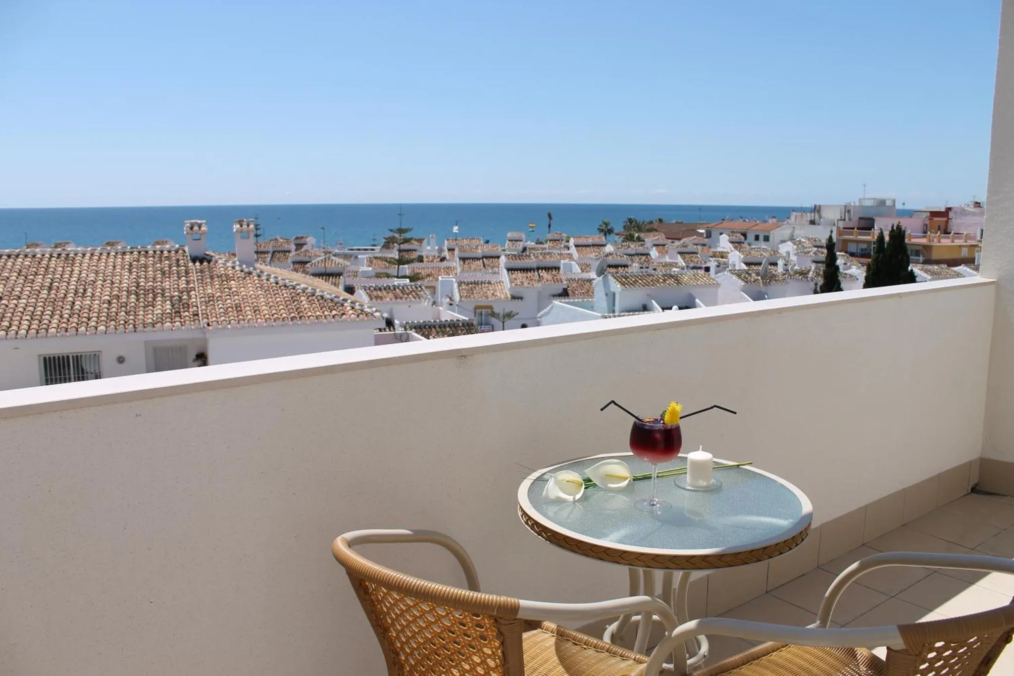 Une table avec des boissons et des chaises sur une terrasse ensoleillée avec vue sur la mer et la ville.