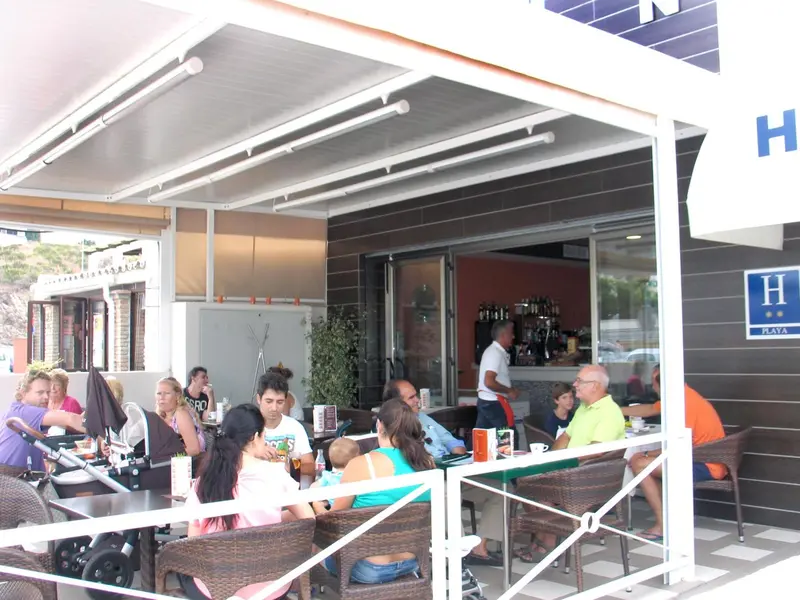 Clients assis à des tables sous une marquise devant un bar.