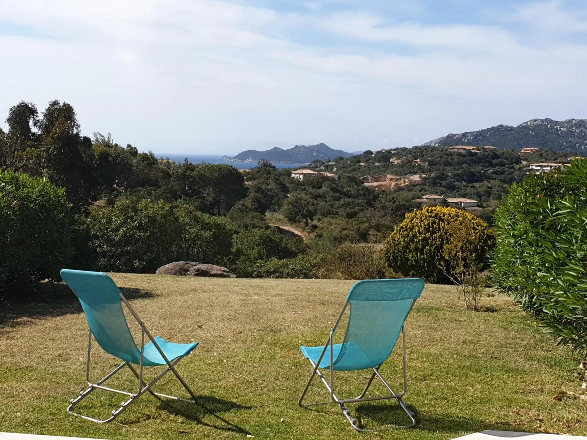 Deux transats bleus sont installés sur une pelouse verdoyante avec vue sur la mer et les collines.