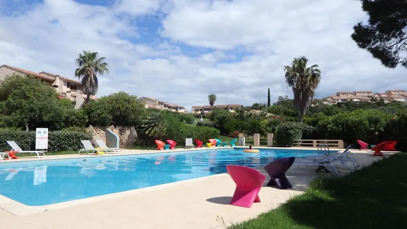 Une piscine bordée de chaises longues et de végétation luxuriante sous un ciel bleu.