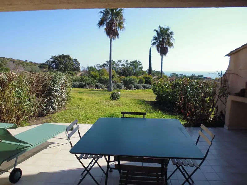 Une table et des chaises sont disposées sur une terrasse carrelée avec vue sur un jardin et la mer.