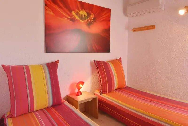 Deux lits simples avec oreillers colorés dans une chambre décorée d'une grande toile.