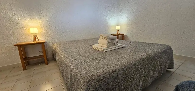 Un lit couvert d'une courtepointe grise est mis en valeur par deux tables de chevet avec des lampes.