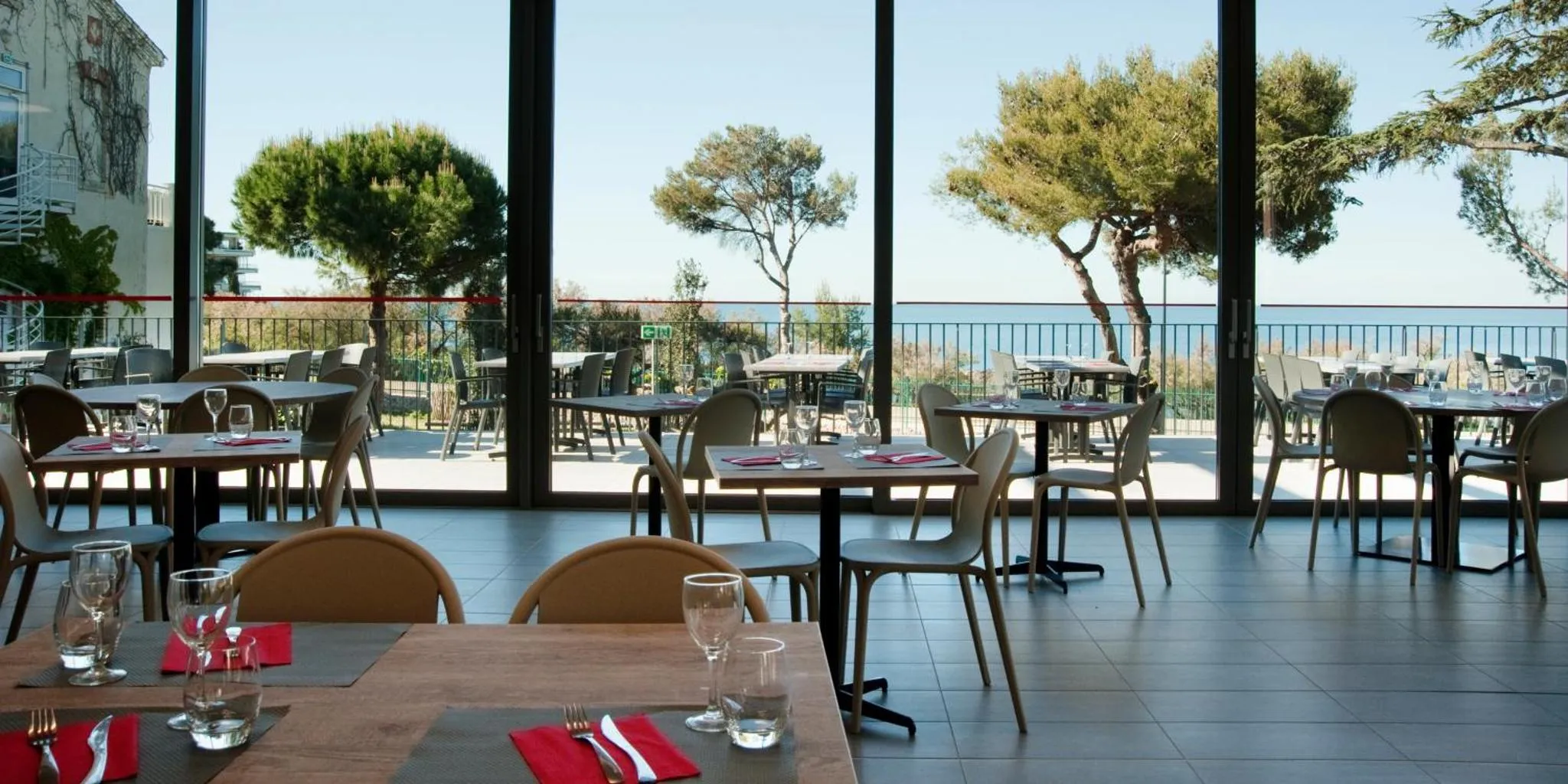 Une salle à manger lumineuse avec des tables dressées face à une vue sur la mer.