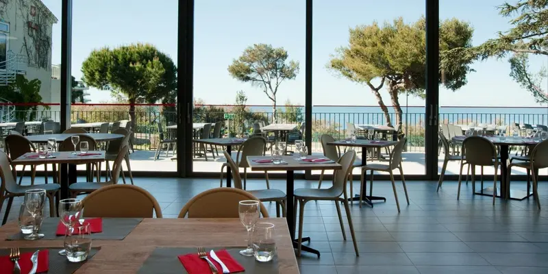 Une salle à manger lumineuse avec des tables dressées face à une vue sur la mer.