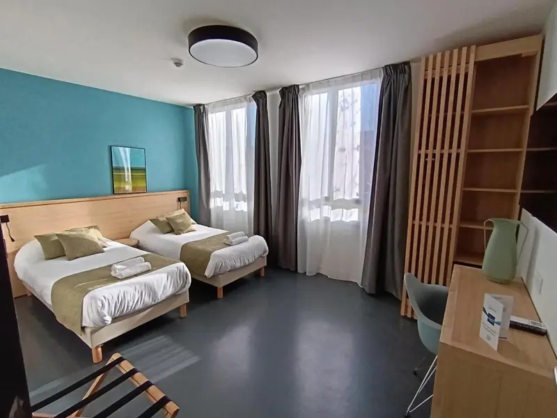 Chambre avec deux lits simples et bureau.