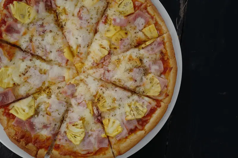Une pizza garnie de jambon et d'ananas est présentée sur une assiette blanche.