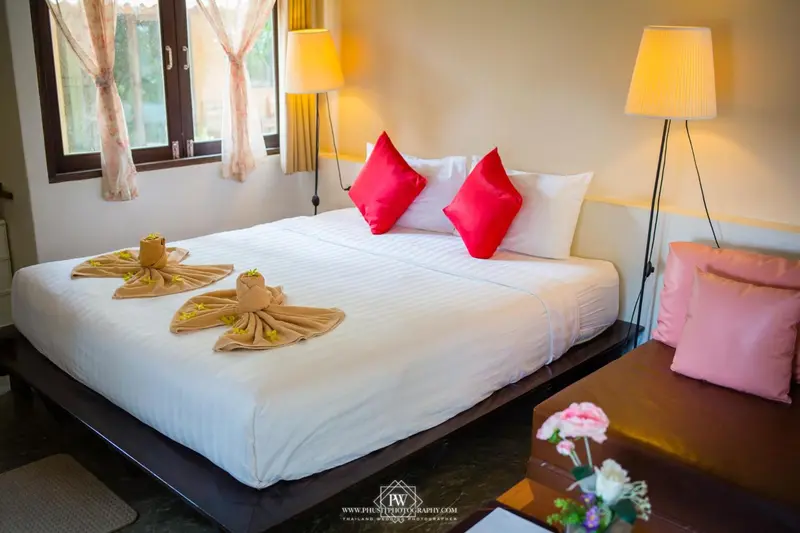 Une chambre lumineuse avec un grand lit recouvert de draps blancs et de coussins rouges.