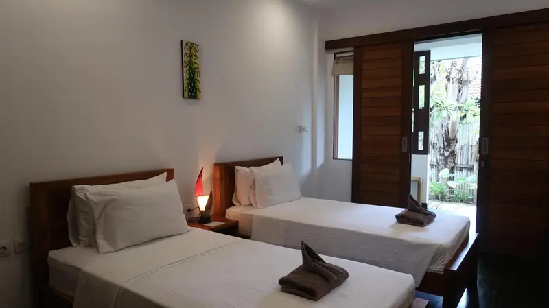 Une chambre lumineuse avec deux lits simples et une porte ouverte sur l'extérieur.