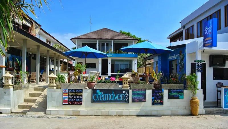 Façade d'un bâtiment blanc avec des parasols bleus et une végétation tropicale.