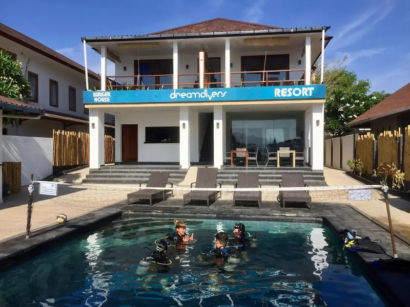 Façade blanche d'un bâtiment avec une piscine au premier plan et des transats.