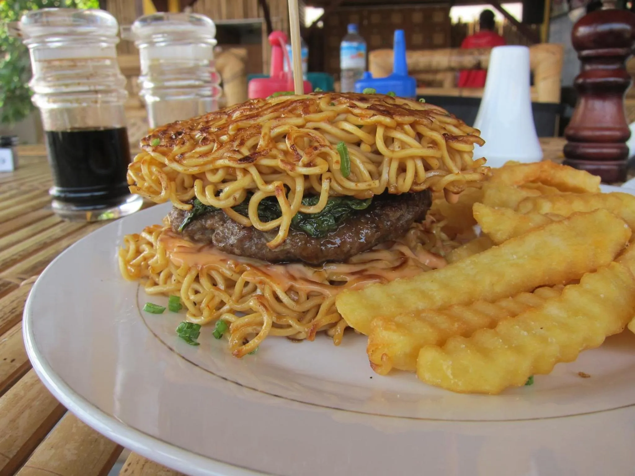 Un plat composé d'un hamburger surmonté de nouilles frites, accompagné de frites.