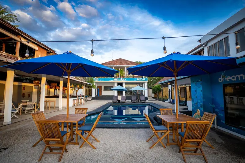 Terrasse ombragée avec tables et chaises près d'une piscine.