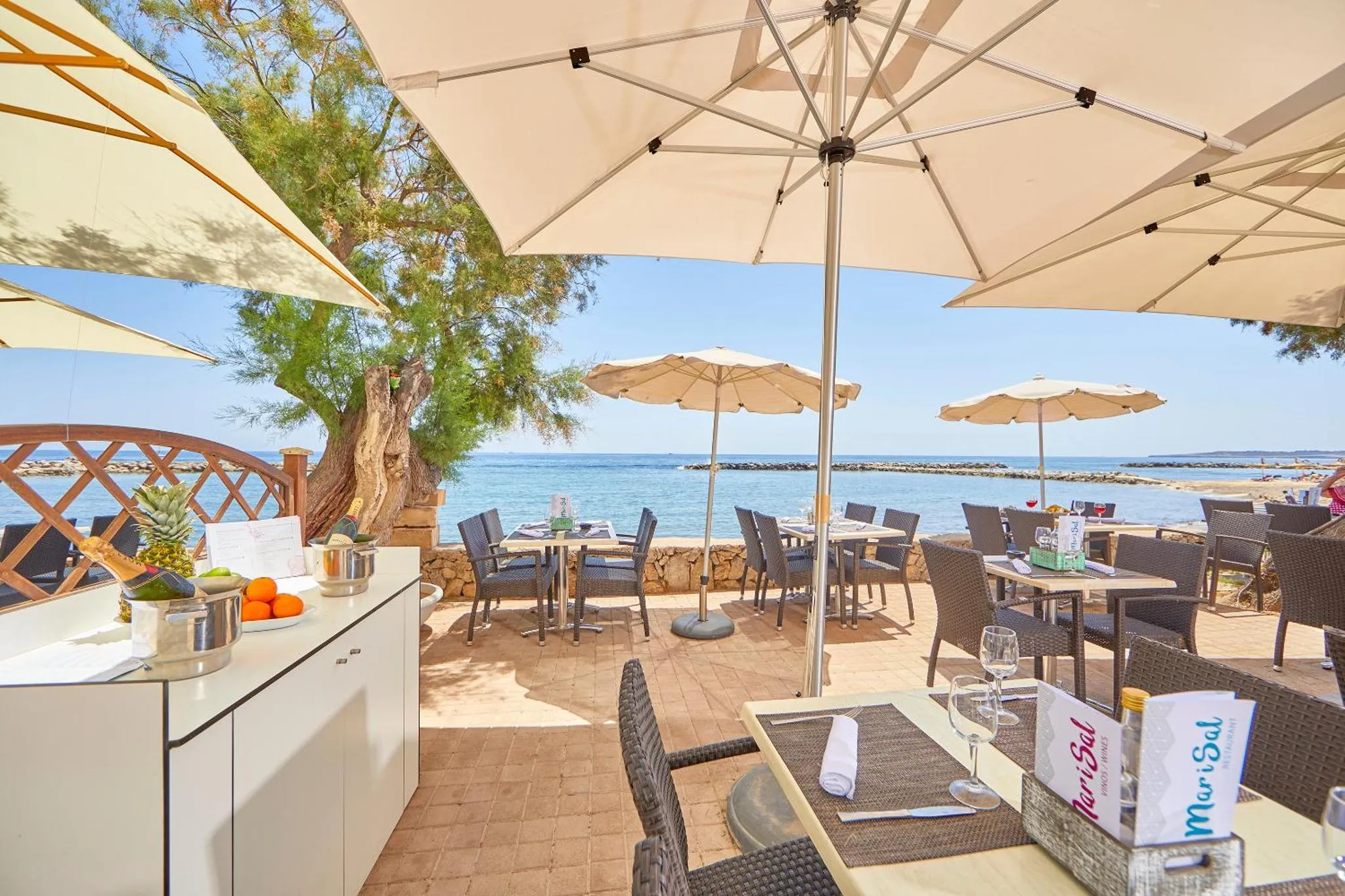 Terrasse ombragée avec tables et chaises en bord de mer.