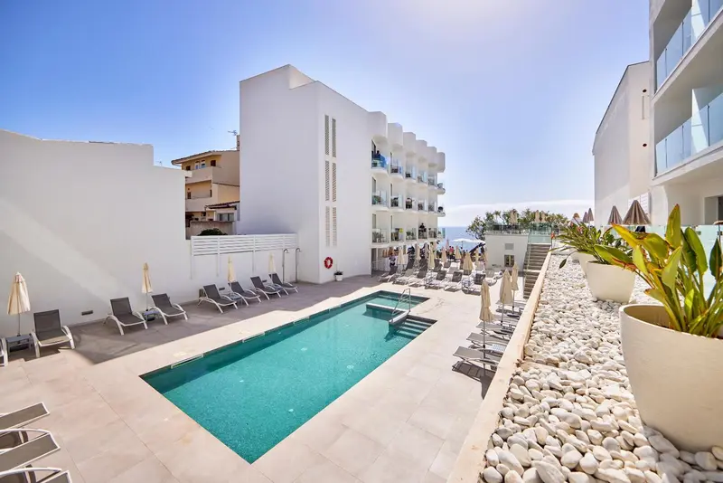 Une piscine rectangulaire bordée de transats et de végétation, devant un bâtiment blanc moderne.
