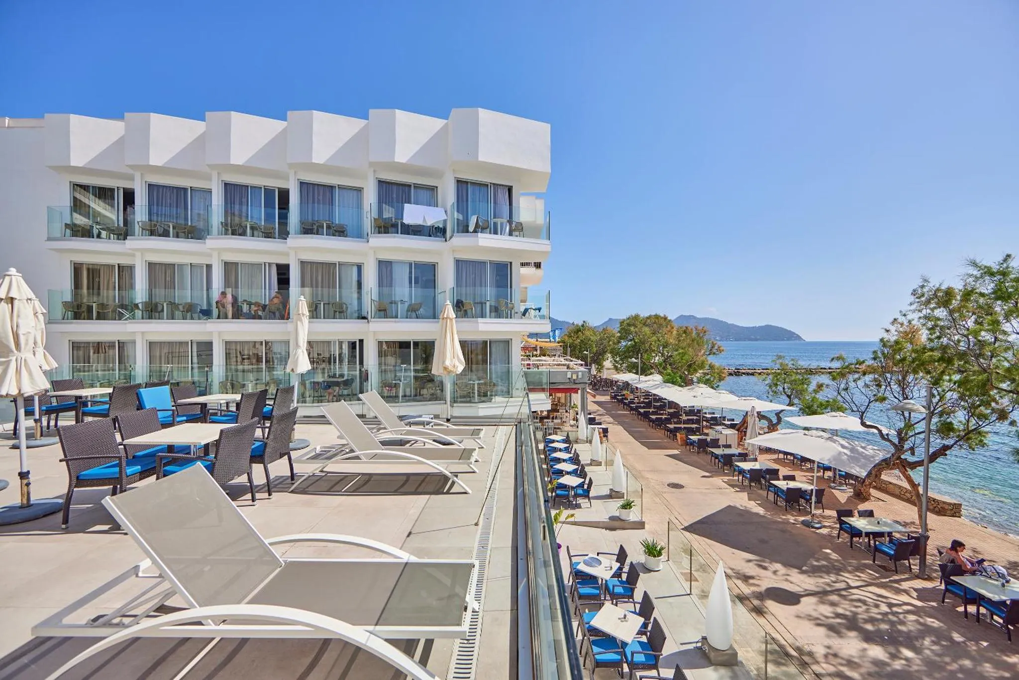 Terrasse ensoleillée avec transats et tables donnant sur la mer.