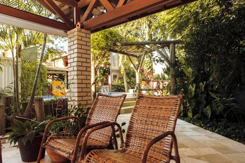 Deux fauteuils en osier sont placés sur une terrasse ombragée avec une végétation luxuriante.