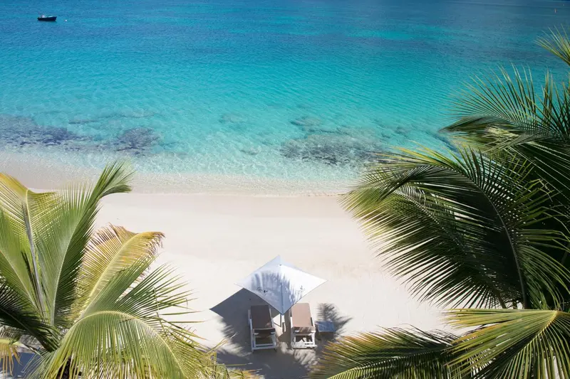 Vue aérienne d'une plage de sable blanc bordée de palmiers et d'une eau turquoise.
