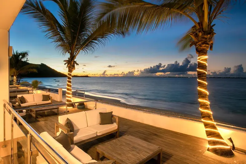 Terrasse lumineuse avec mobilier blanc face à la mer au coucher du soleil.