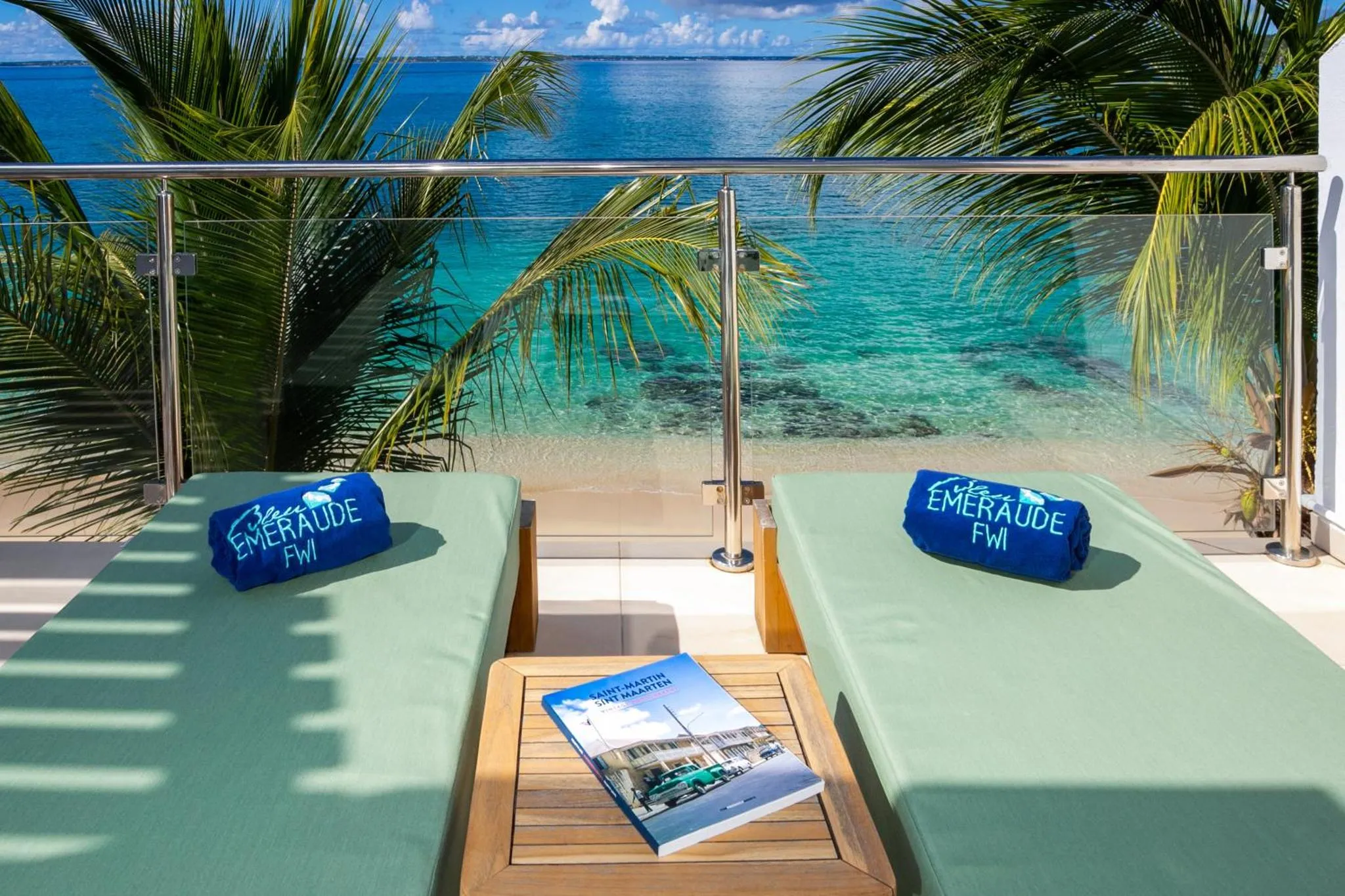 Transats verts sur une terrasse avec vue sur la mer turquoise et une plage de sable blanc.