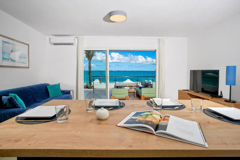 Une table est dressée devant un canapé et un téléviseur, avec vue sur la mer par une baie vitrée.