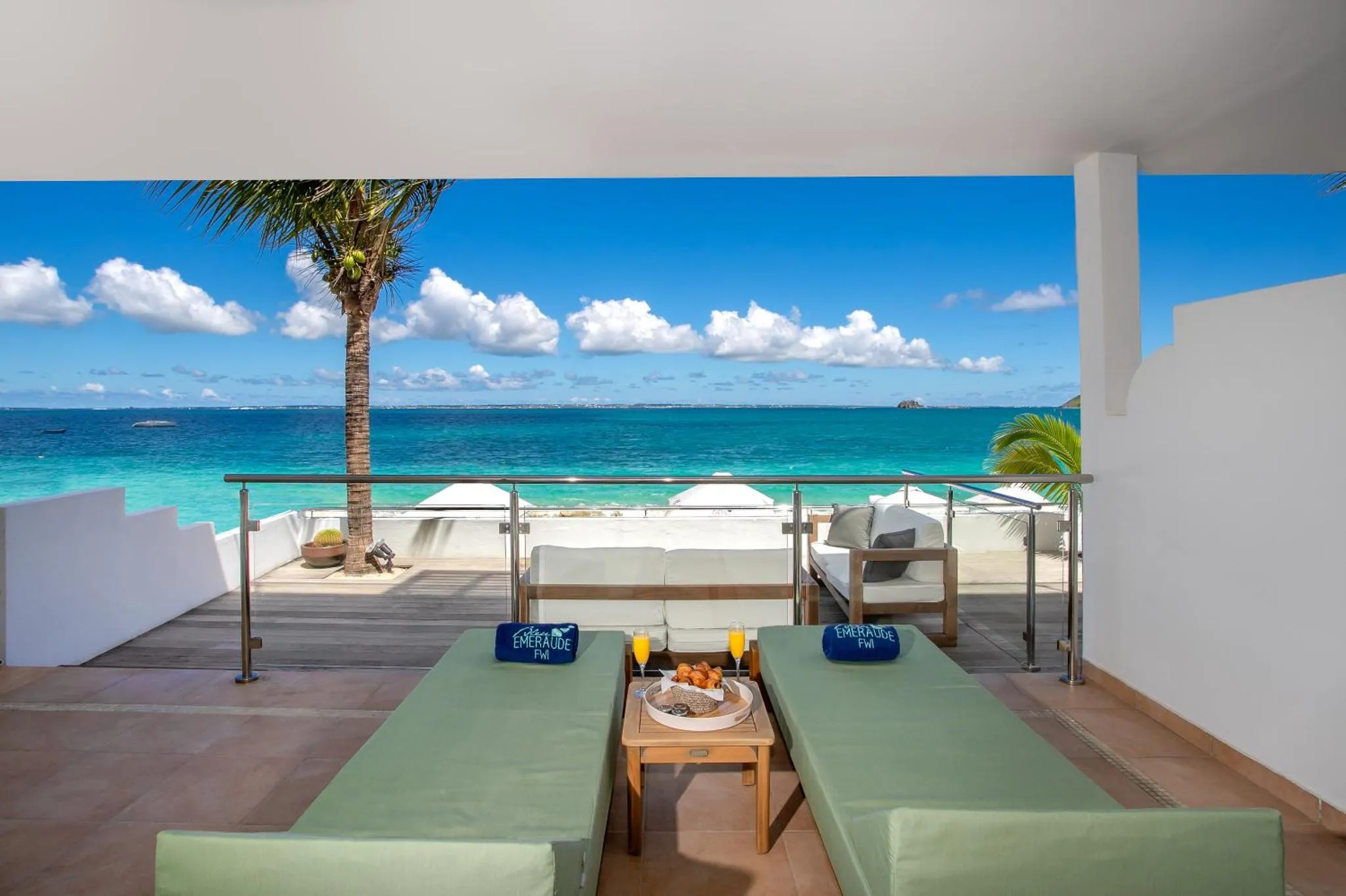 Deux transats et une table basse avec des boissons et des fruits sur une terrasse ensoleillée avec vue sur la mer.