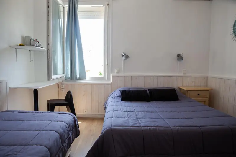 Une chambre lumineuse avec deux lits simples et un lit double.
