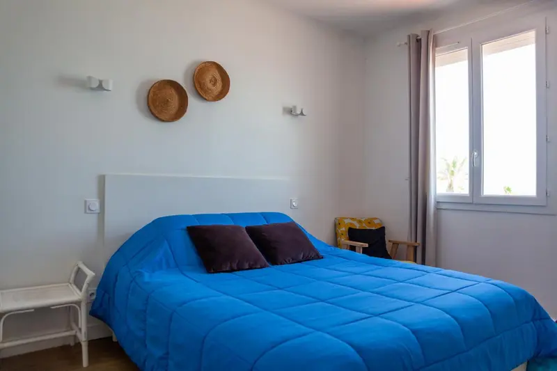 Une chambre lumineuse avec un grand lit recouvert d'une couverture bleue.