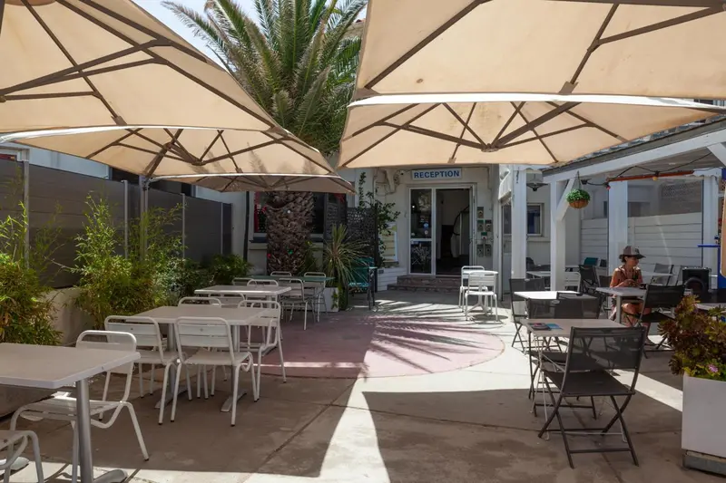 Terrasse ombragée avec tables et chaises devant un bâtiment blanc.