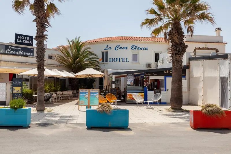 Façade d'un hôtel avec des palmiers et des tables de terrasse.