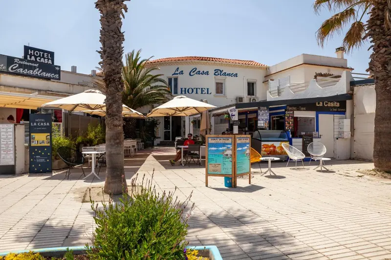 Façade d'un hôtel avec une terrasse ombragée et des tables.
