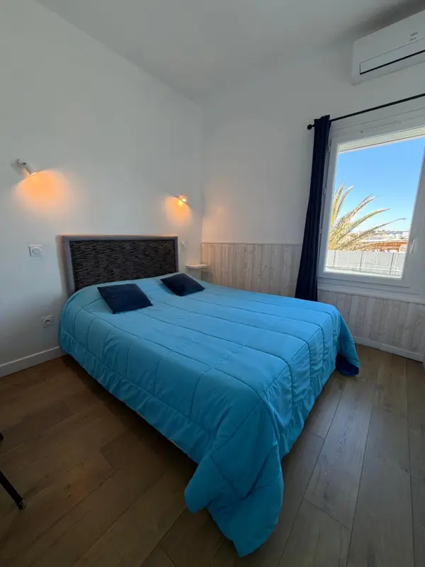 Chambre lumineuse avec un grand lit recouvert d'une couverture bleue.