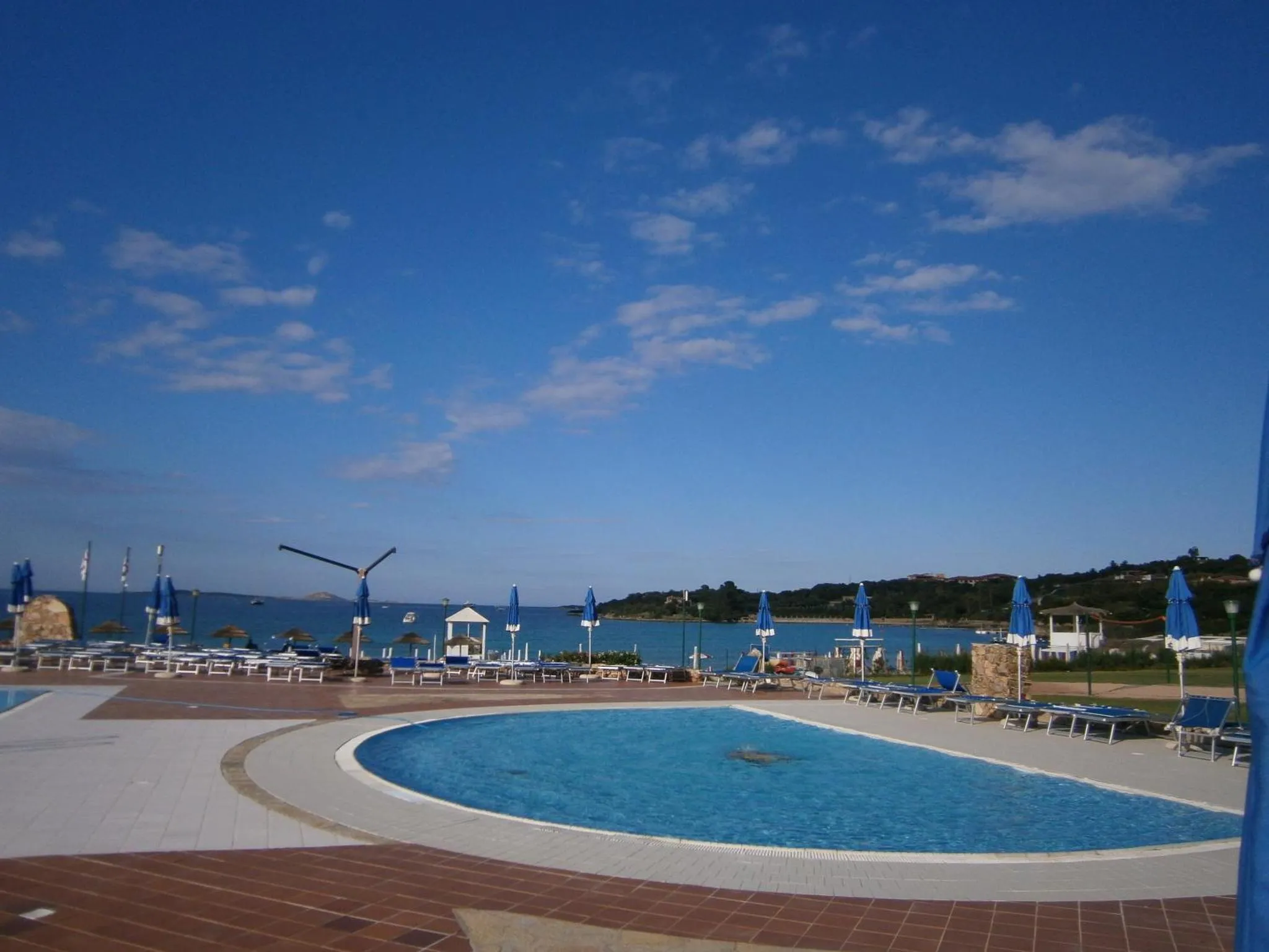Une piscine avec des transats et des parasols en bord de mer sous un ciel bleu.