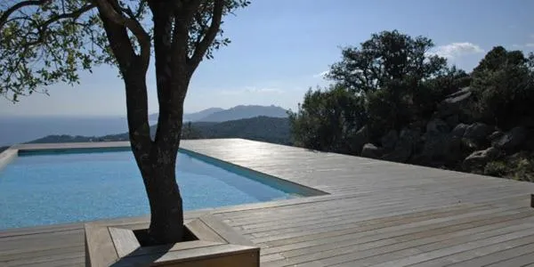 Une piscine rectangulaire bordée d'une terrasse en bois offre une vue sur la mer et les montagnes.