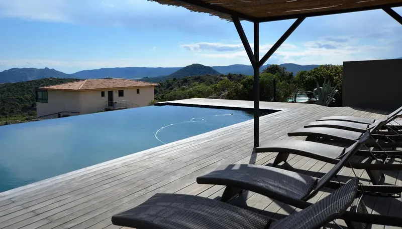 Terrasse avec piscine à débordement et chaises longues face à un paysage montagneux.