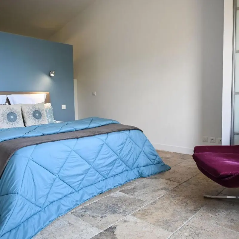 Une chambre lumineuse avec un grand lit recouvert d'une couette bleue et des oreillers décorés.