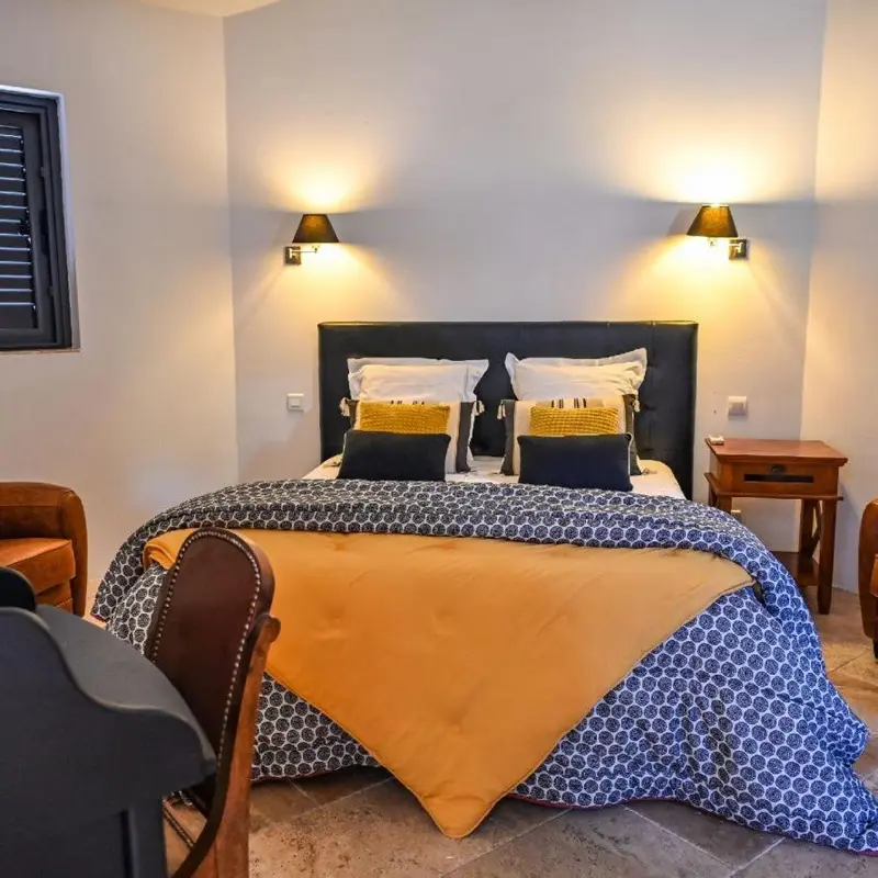 Une chambre lumineuse avec un grand lit recouvert d'une courtepointe jaune et bleue.