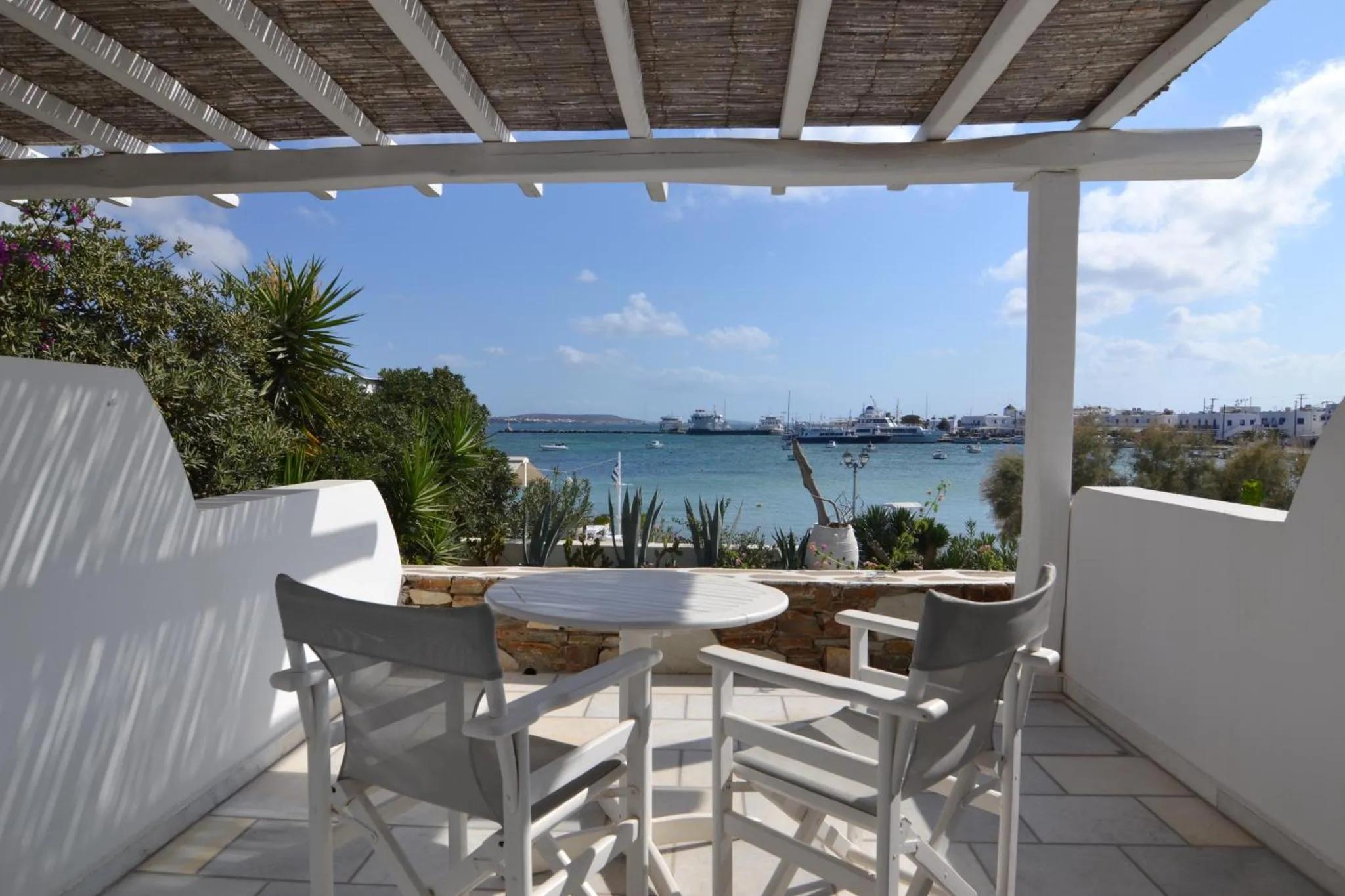 Terrasse ombragée avec table et chaises donnant sur la mer.